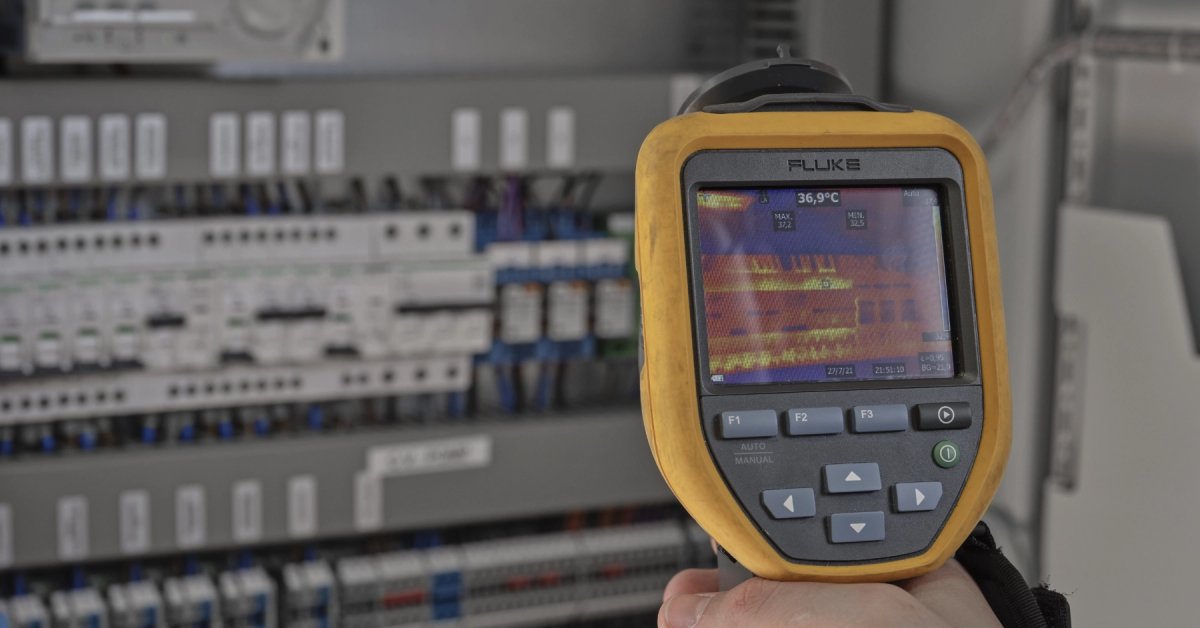 Hand houdt een thermische camera voor een elektrische verdeelkast.